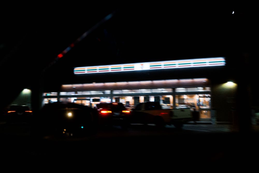 Passing a convenience store at night, the photo is framed by my car window and side mirror