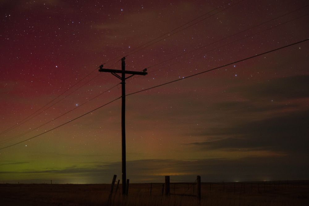 A power line pole in front of the northern lights in the night shot