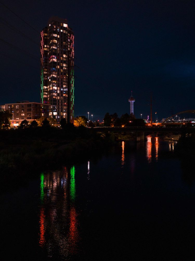A tall building with colorful lights is reflected in the water of a river. 