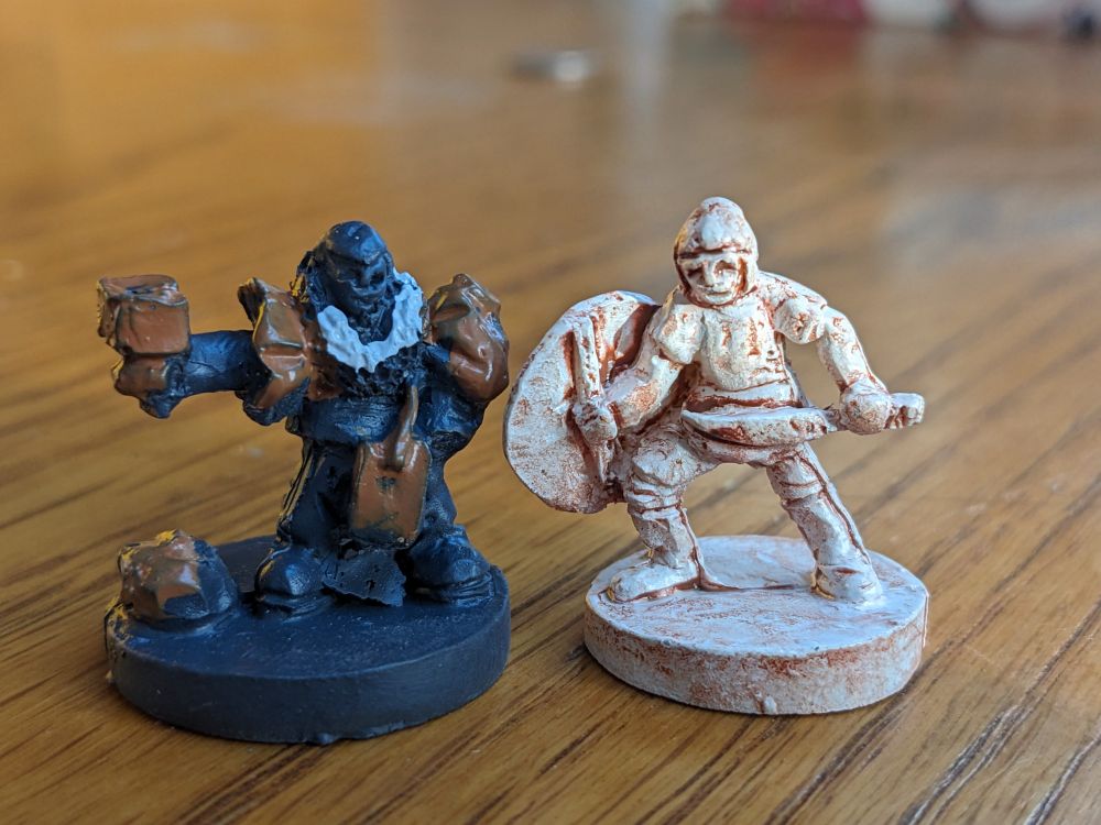 Two gaming figurines. On the right a terracotta- looking warrior, on the left some misshapen black figure with what could be a white beard.