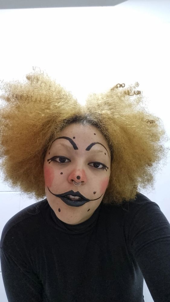 Foto minha com a maquiagem de palhaço, blusa lisa de gola alta preta e fundo branco.
