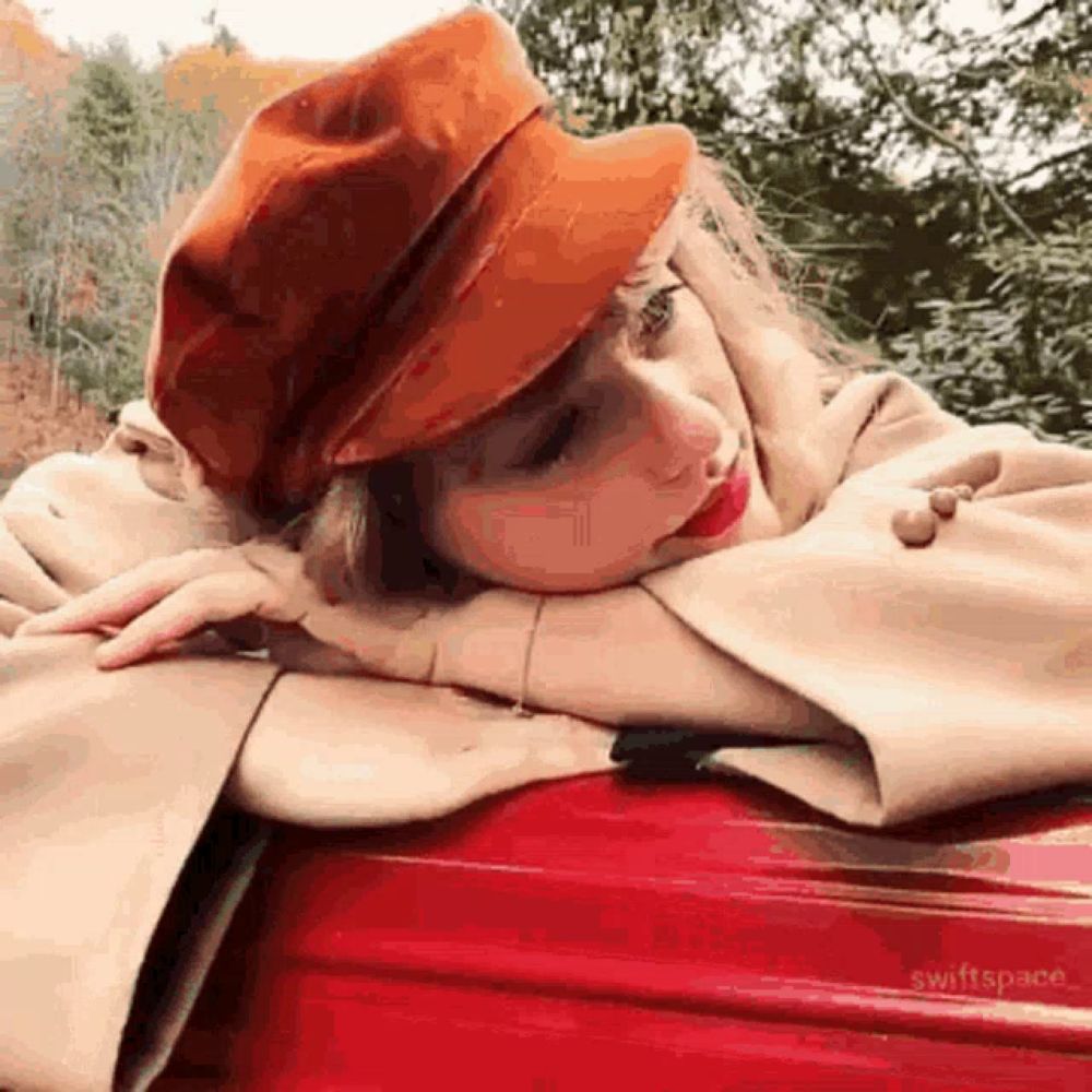 a woman wearing a hat and a coat is laying on top of a red car .