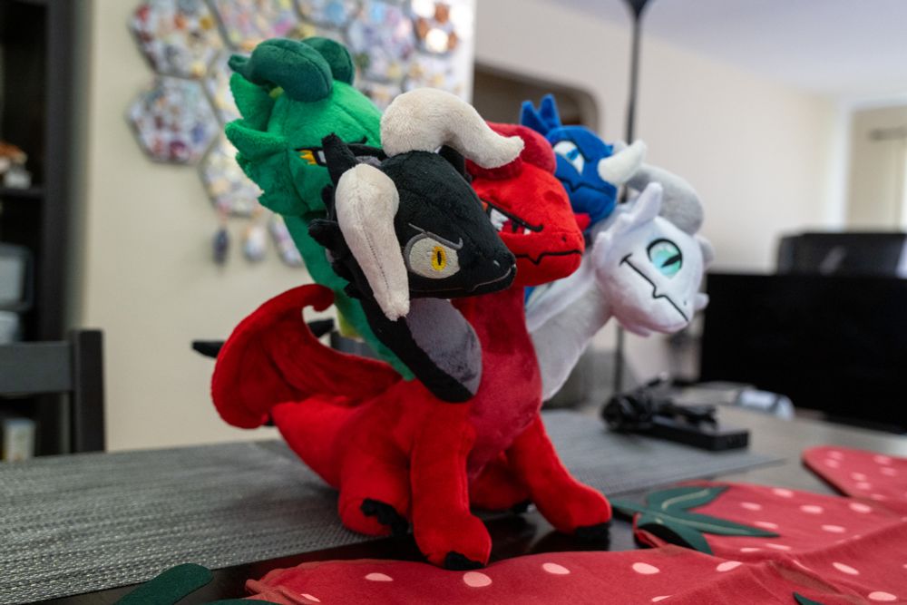 a side-front view of a five headed dragon plush. the body is red, and the heads are, from left to right, black, green, red, blue, and white.