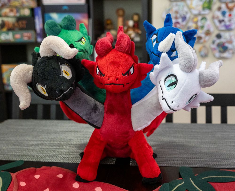 a front view of a five headed dragon plush. the body is red, and the heads are, from left to right, black, green, red, blue, and white.
