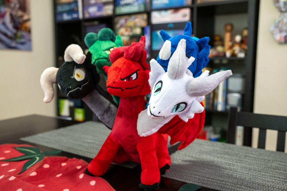 a side-front view of a five headed dragon plush. the body is red, and the heads are, from left to right, black, green, red, blue, and white.