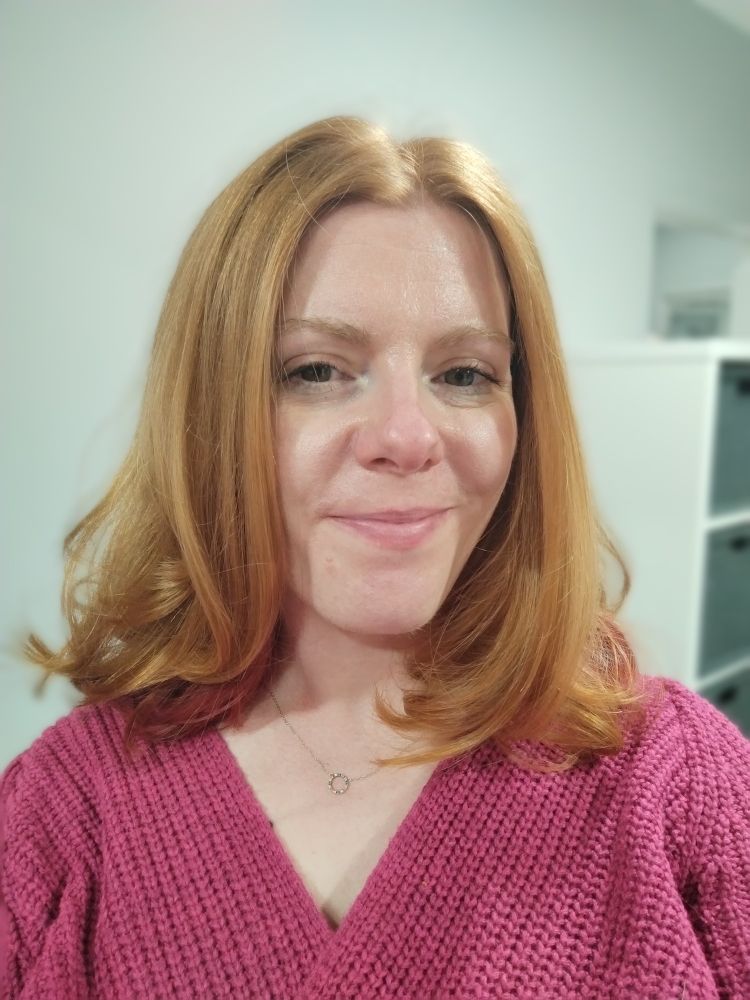 A Tora in a pink jumper and hair cut to shoulder length.