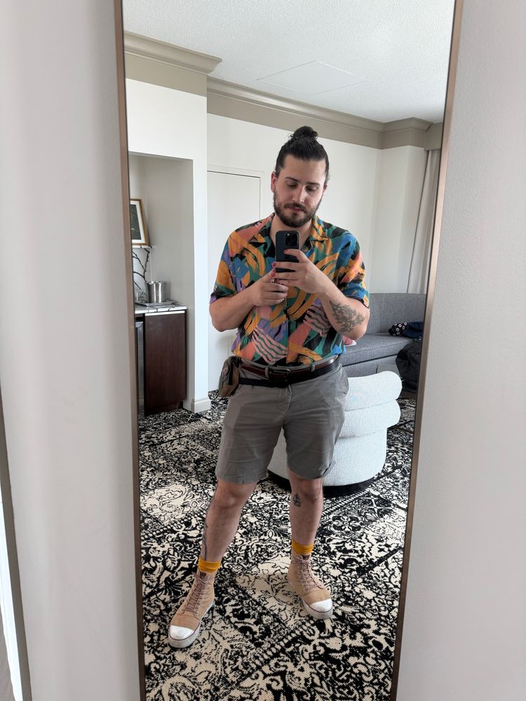 Mirror selfie of Elliot in a hotel room wearing a summer-y outfit featuring and orange patterned shirt