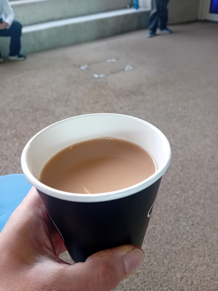 A white hand holding a take away cup of tea.