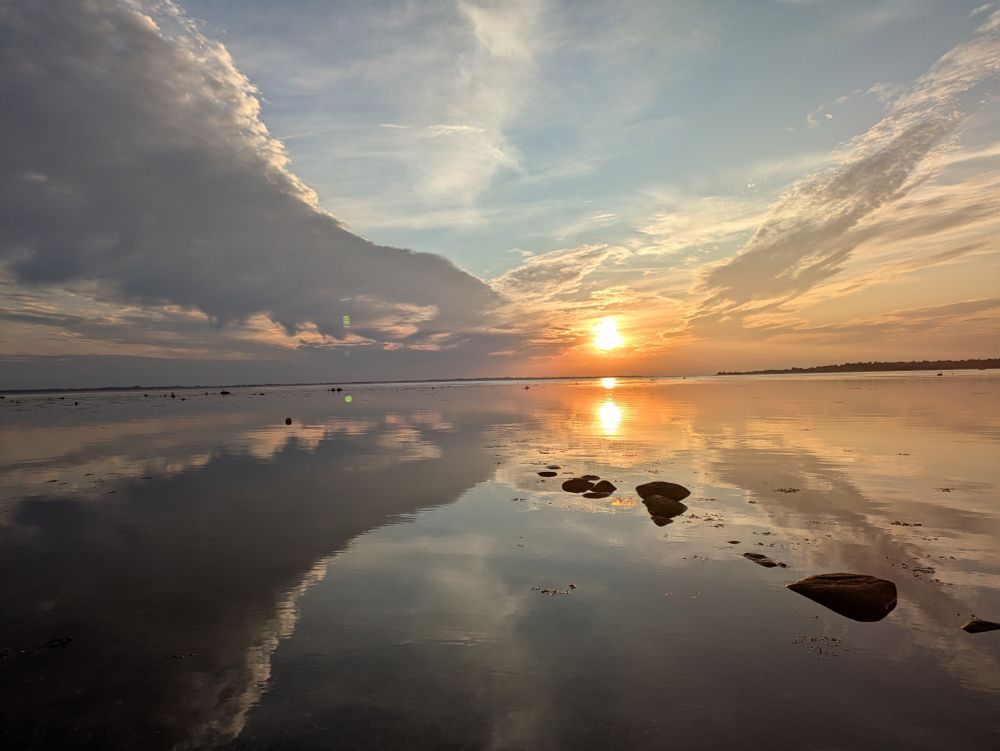 Eine tiefstehende Sonne über Wasser. Der Himmel spiegelt sich im Wasser.