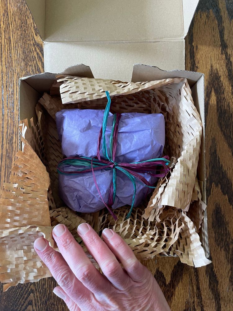Unboxing the package to find a beautifully wrapped parcel with lavender tissue paper tied with teal and burgundy raffia 