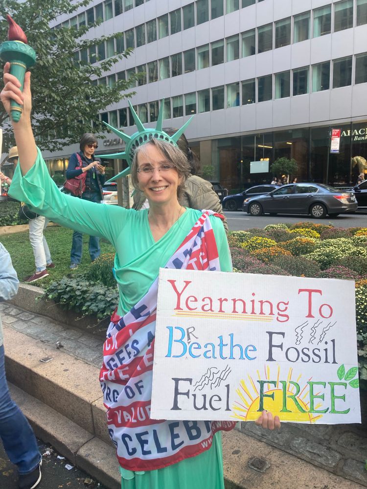 An activist dressed as the statue of liberty holding a sign against fossil fuels