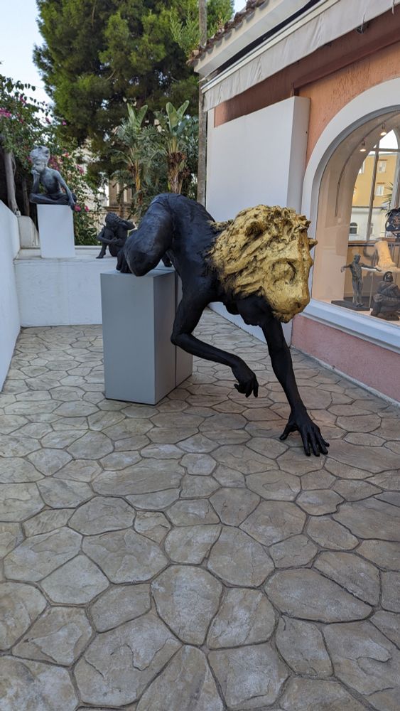 Dark naked human figure wearing gold lion head crawling off of a pedestal