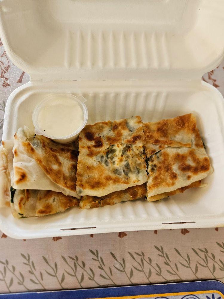 The Cheese & spinach gözleme cut into squares in a cardboard takeaway box. 