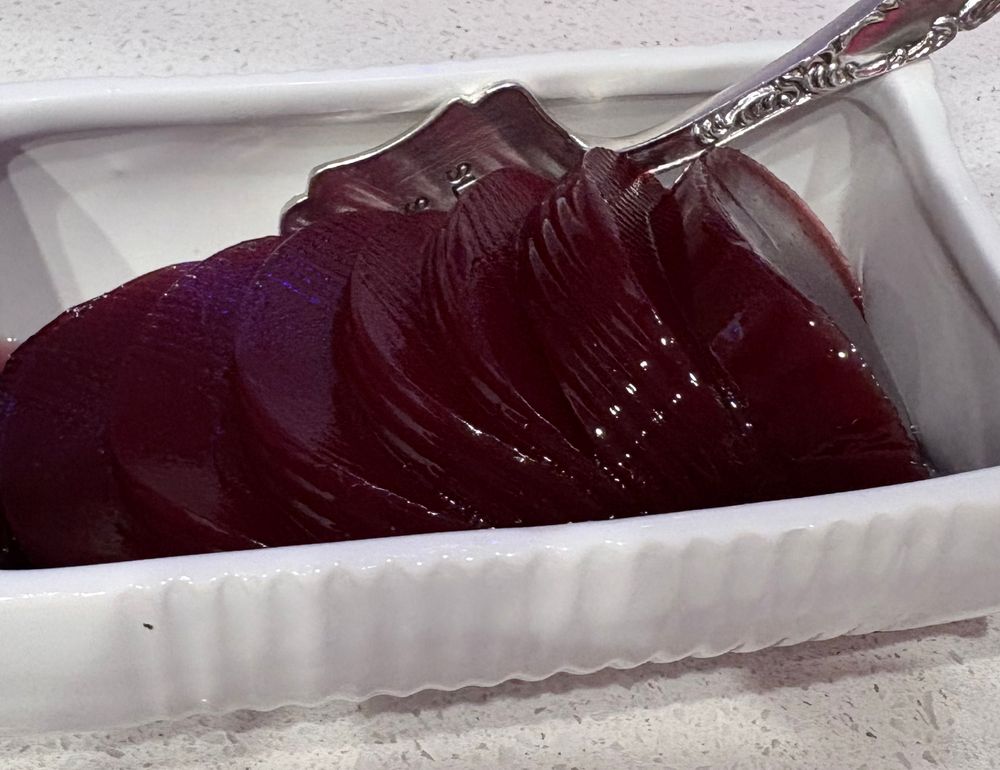 A “jellied cranberry serving dish” with sliced jellied cranberry in it, waiting to be served with a small silver spatula 