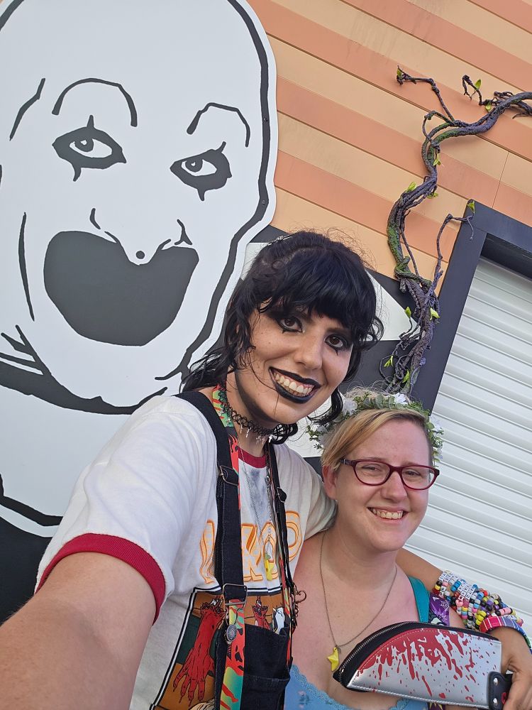 A selfie of me (left) and my beautiful fiance (Percy, right) smiling as I hold my knife purse to his neck. To the left there's an illustration of Art the clown.