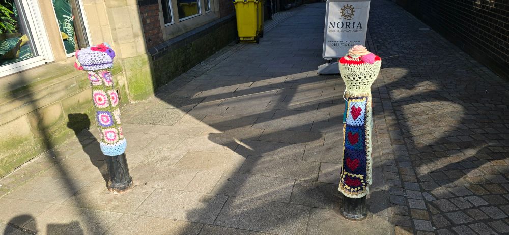 Two bollards in Altrincham with knitted colourful covers rather incongruously places on them.