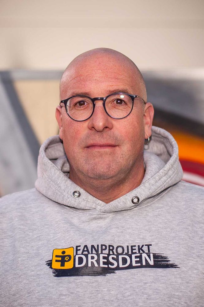 Christian Kabs lächelt milde in die Kamera, er trägt einen grauen Kapuzenpullover mit dem Aufdruck "Fanprojekt Dresden".