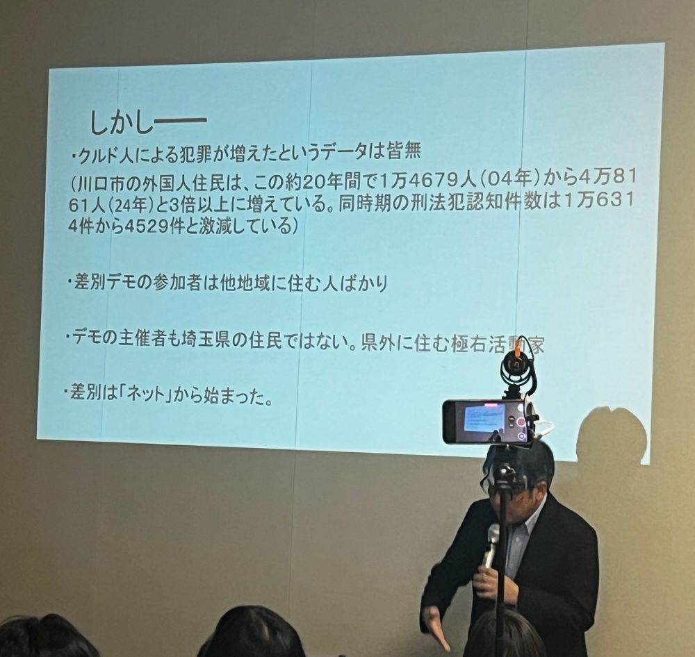 "しかし
・クルド人による犯罪が増えたというデータは皆無（川口市の外国人住民は、この約20年間で1万4679人（04年）から4万81
61人（24年）と3倍以上に増えている。同時期の刑法犯認知件数は1万6314件から4529件と激減している）
・差別デモの参加者は他地域に住む人ばかり
・デモの主催者も埼玉県の住民ではない。
県外に住む極右活動家
・差別はネットから始まった。"

というスライドの前に立つ安田浩一さん