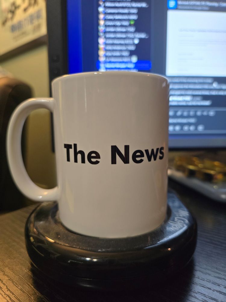 A white coffee mug that says The News sits on a coffee warmer. 
