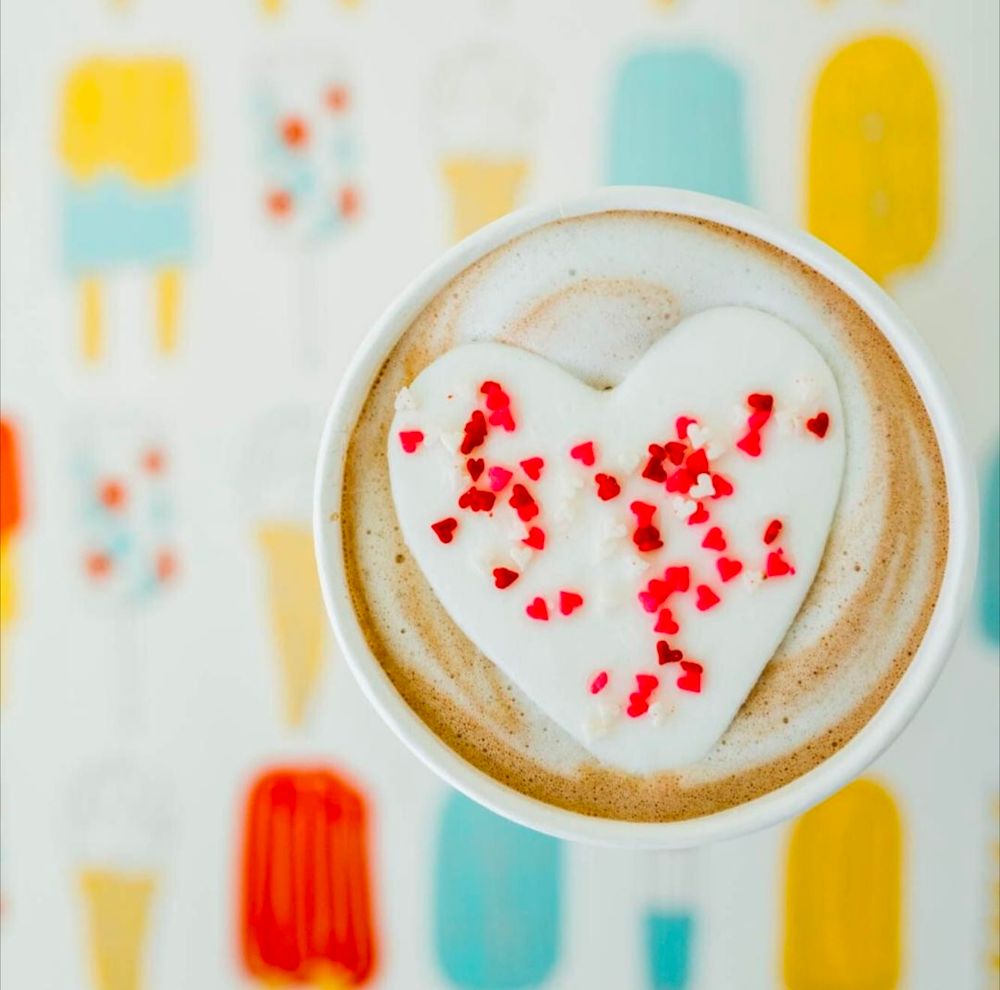 Picture of a cup of hot coco shot from above with a heart shaped marshmallow and red sprinkles in the cup. 