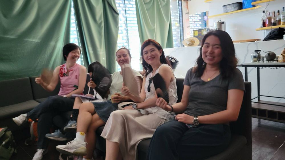 Four ladies sitting in a row with handheld folding fans. 