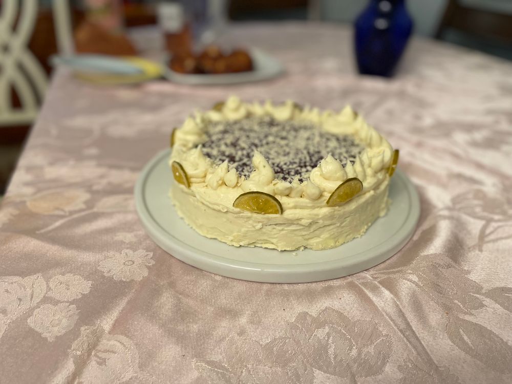 Photograph of a cake on a white plate, in a pink tablecloth. It is a guava cake filled with guava paste and lime curd, decorated with coconut buttercream, guava paste, toasted coconut and candied lime