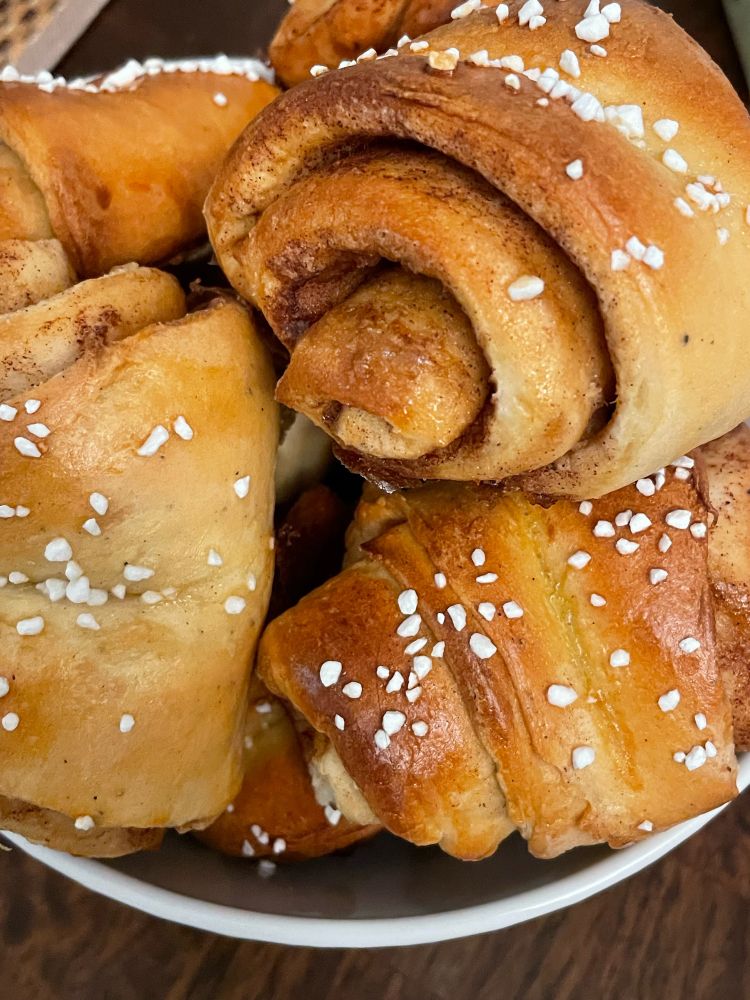 Photograph of a pile of Finnish cinnamon rolls, called korvapuustit, in a while bowl on a brown table