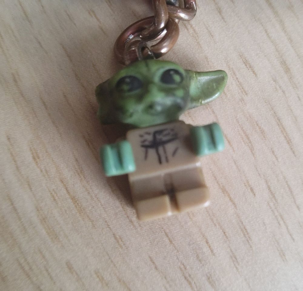 Un porte-clés LEGO Grogu, un petit alien vert avec des longues oreilles, une de ses oreilles est cassée