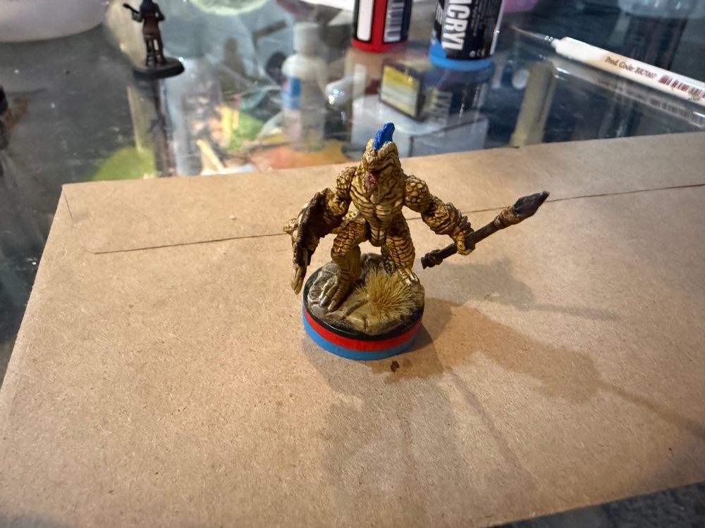 A lizardman miniature standing on a red disk stacked on top of a blue disk.