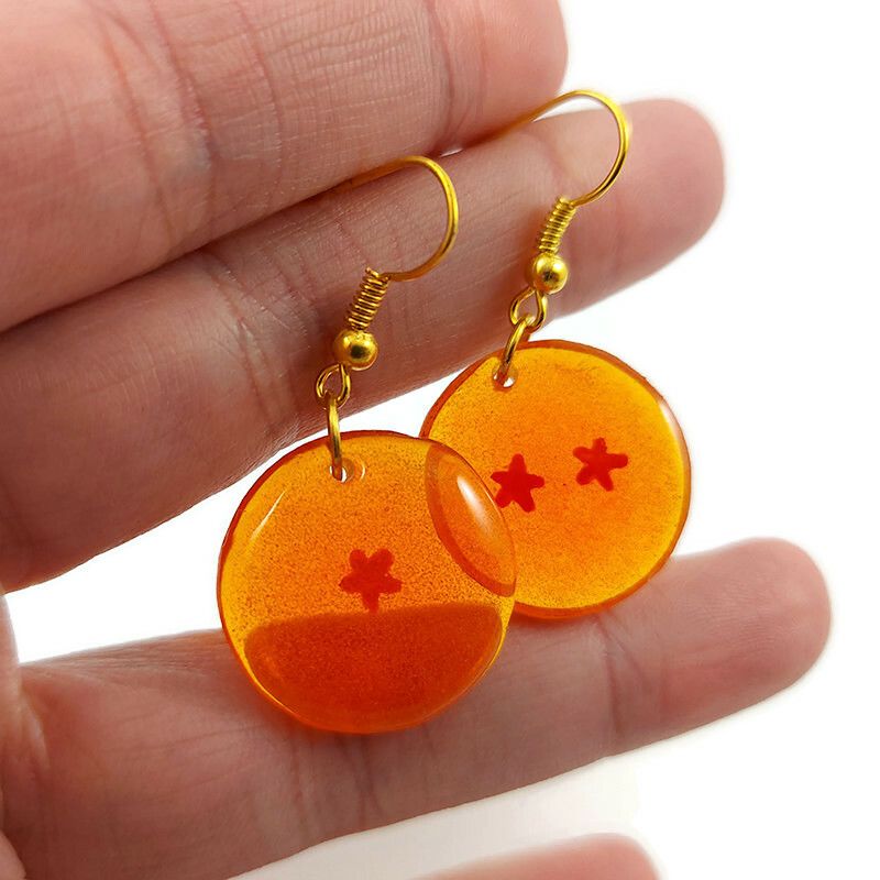 Boucles d'oreilles fantaisie pendantes éco-responsables en forme de Dragon Ball avec 1 et 2 étoiles.
Les perles sont réalisées en CD recyclé, découpées et peintes à la main, puis recouvertes de résine époxy teintée orange.
Les attaches sont en laiton doré, mais sont aussi disponibles dans d'autres métaux et coloris.
