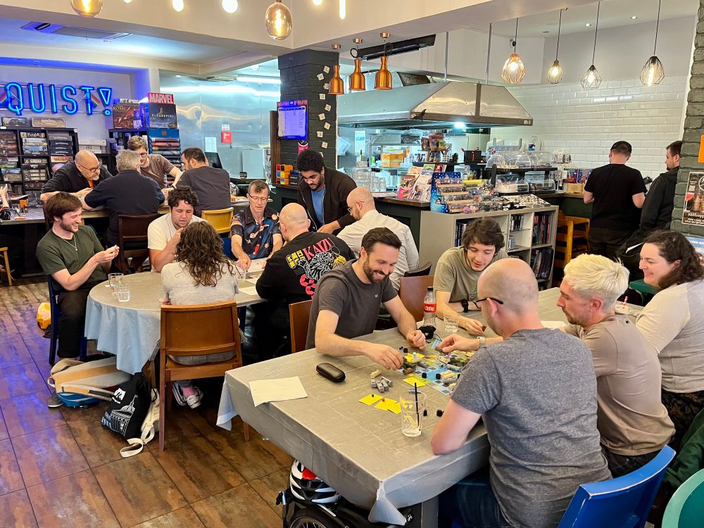 A picture of a number of people sat at tables in a board game cafe, playing board game prototypes. 