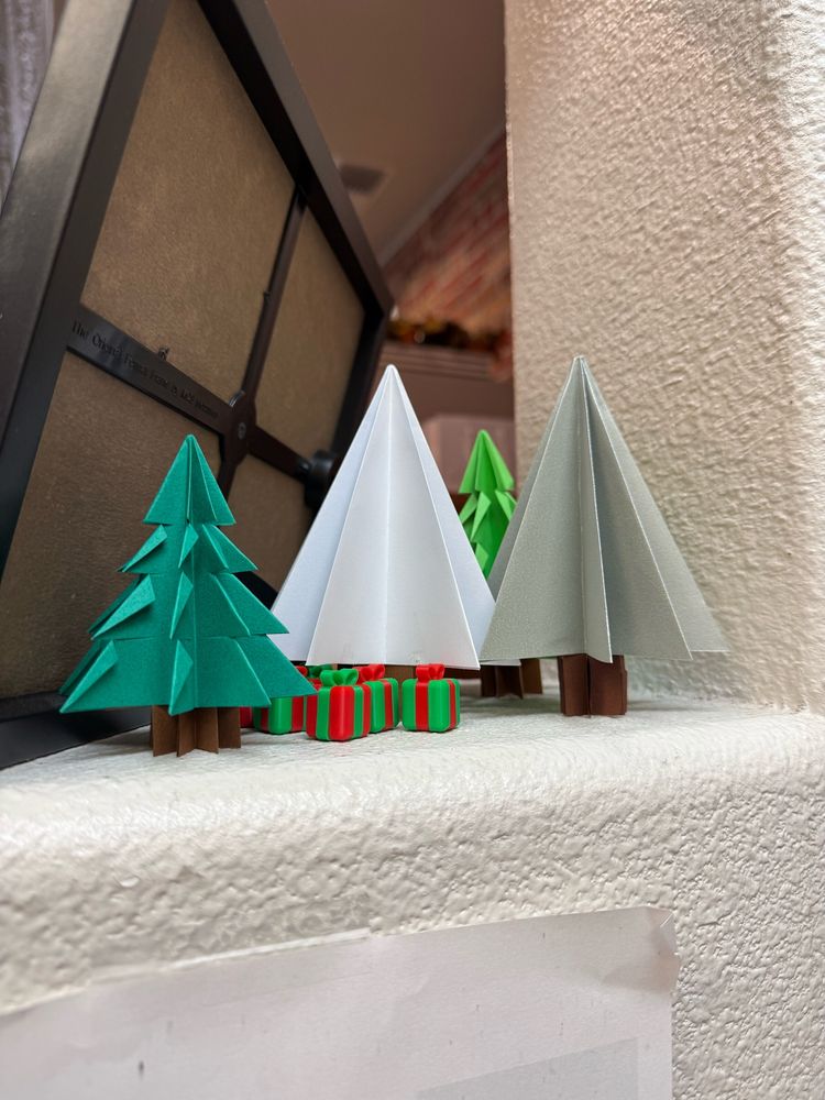 several folded paper trees in with tiny red and green gift boxes under them