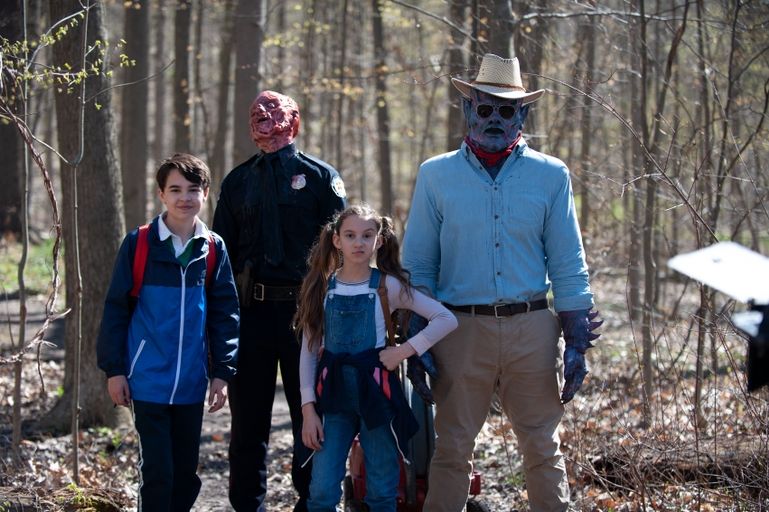 Psycho Goreman wearing a blue shirt, tan pants, a red bandana & a cowboy hat 