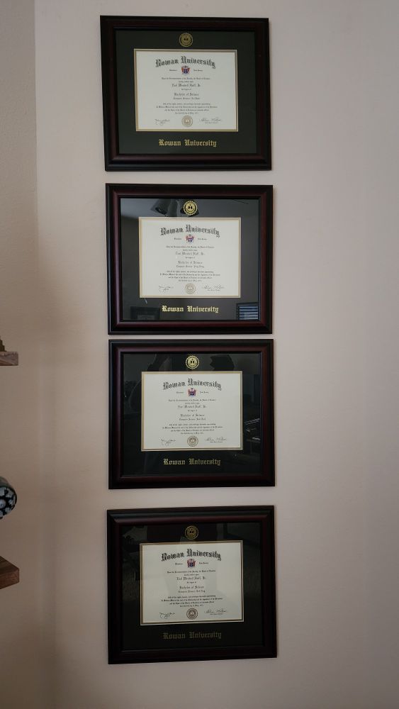 Four bachelor's degree diplomas hanging on a wall, vertically in alignment.