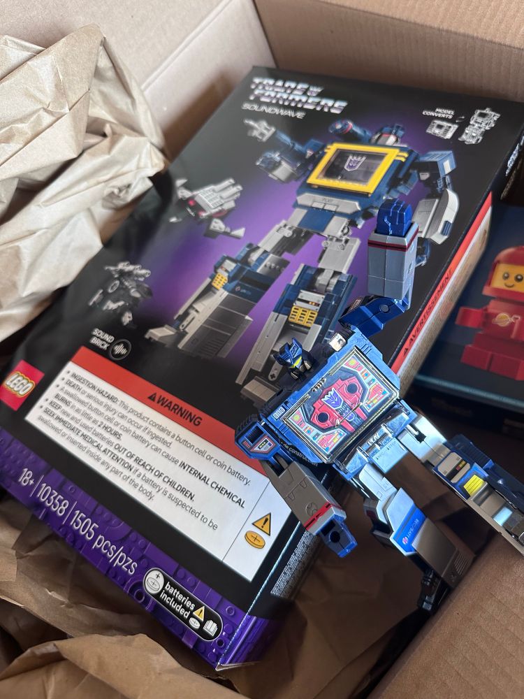 A Lego set for Soundwave, the cassette player Transformer. In the foreground is the toy that the set is based on. In the background is the current bonus set when ordering directly from Lego, a chibi astronaut. 