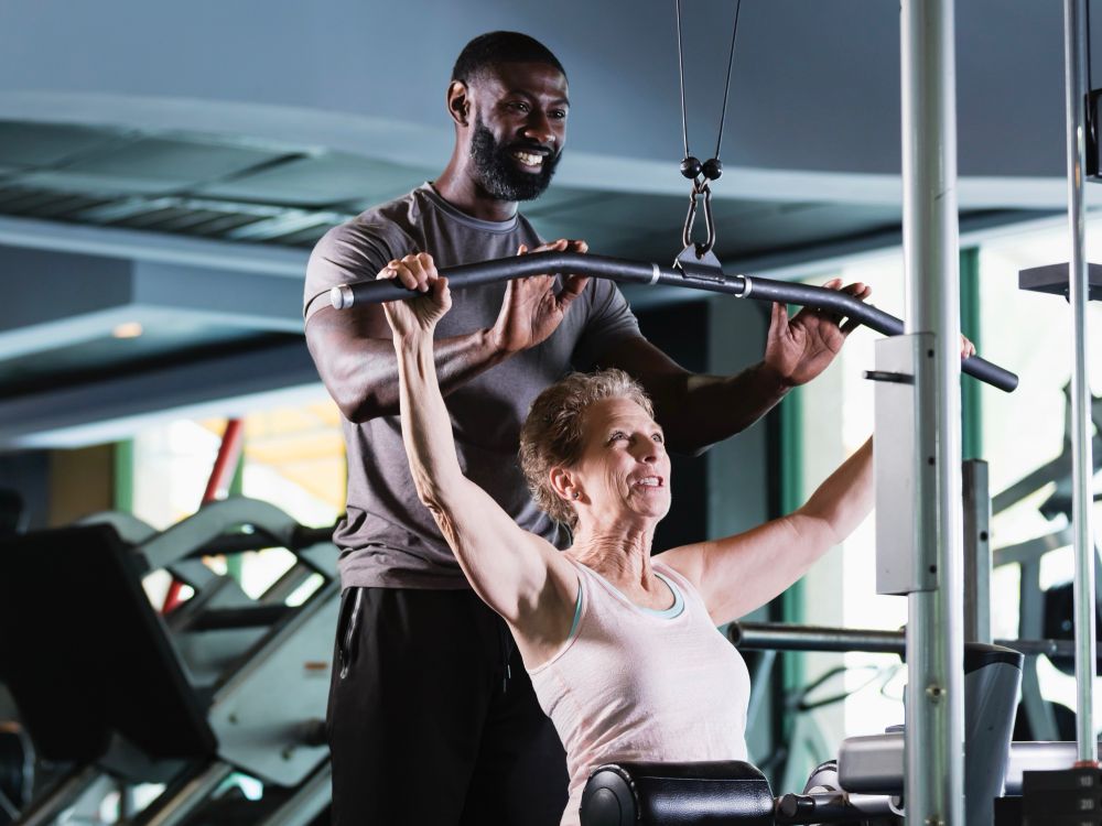 A tall personal trainer helping an older woman with her exercise regimen. 