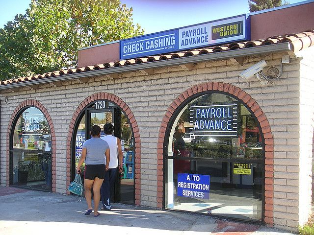 The same building from the previous image that is now a check cashing location, with glass windows and door retrofitted into the brick archways. 