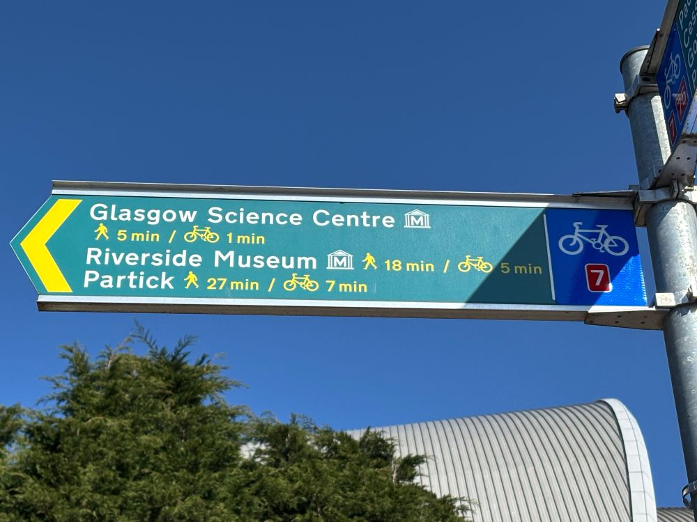 View of finger post sign against a beautiful blue sky giving directions including walking and cycling times with pictograms for a human walking and a cycle 