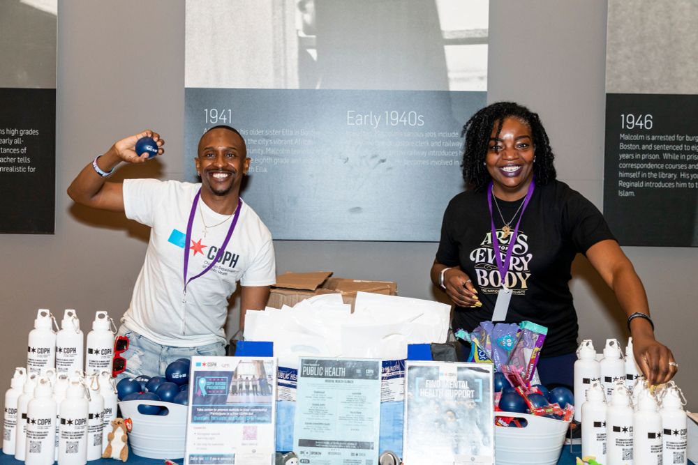 Two people smiling, standing at a table displaying bottles and other resources.