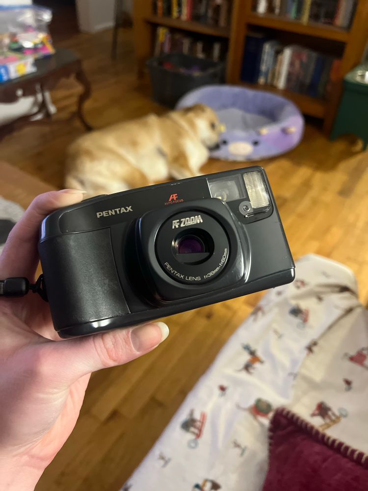 picture of me holding a Pentax IQZoom 60 camera. there’s a gold dog sleeping on the floor in the background.