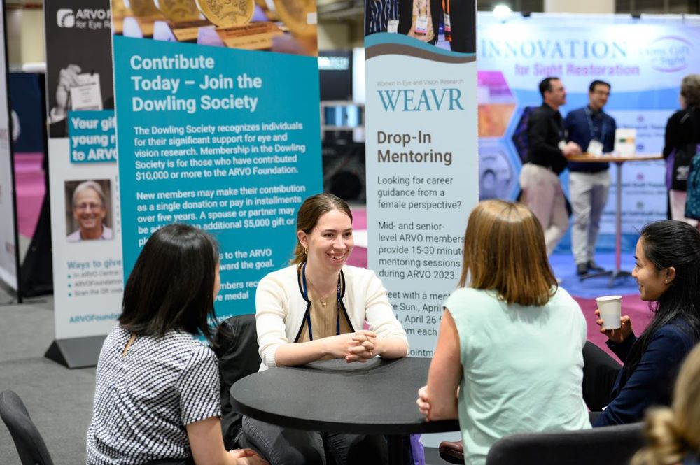 Three ARVO attendees seated at a table in discussion with a WEAVR mentor