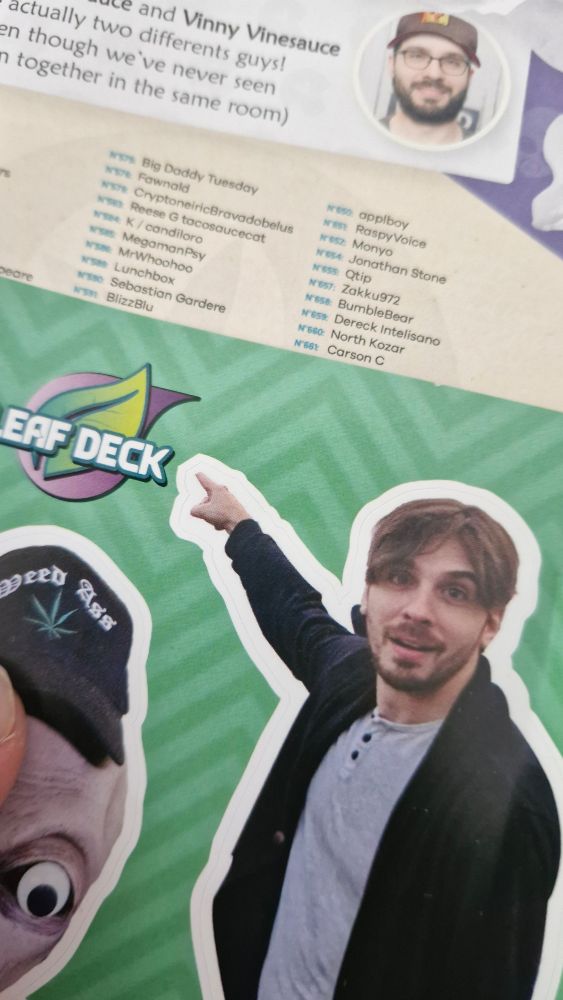 a photo of the booklet that came with the Vinesauce Trading Card Collection, open on a page with my username listed on it; on top lays a Vinny sticker on a sticker sheet, indirectly pointing at the username
