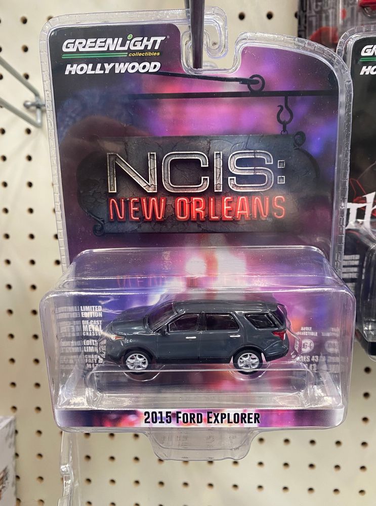 A Hot Wheels-style car from Greenlight Collectibles depicting a gray 2015 Ford Explorer under the "NCIS: New Orleans" logo on the package. The toy hangs on a peg in the Walmart toy aisle.