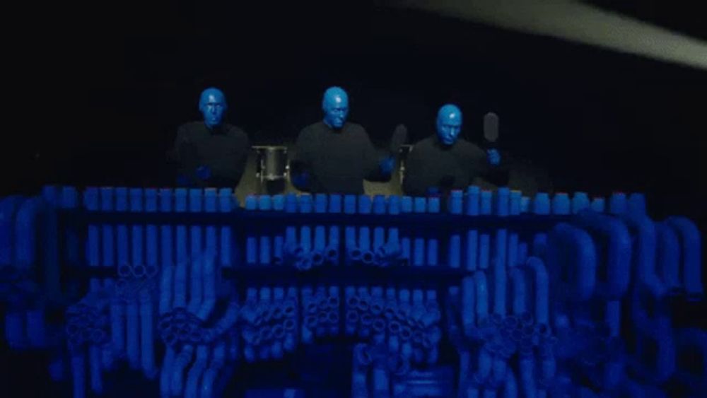 a group of blue men are playing drums in front of a display of blue cups