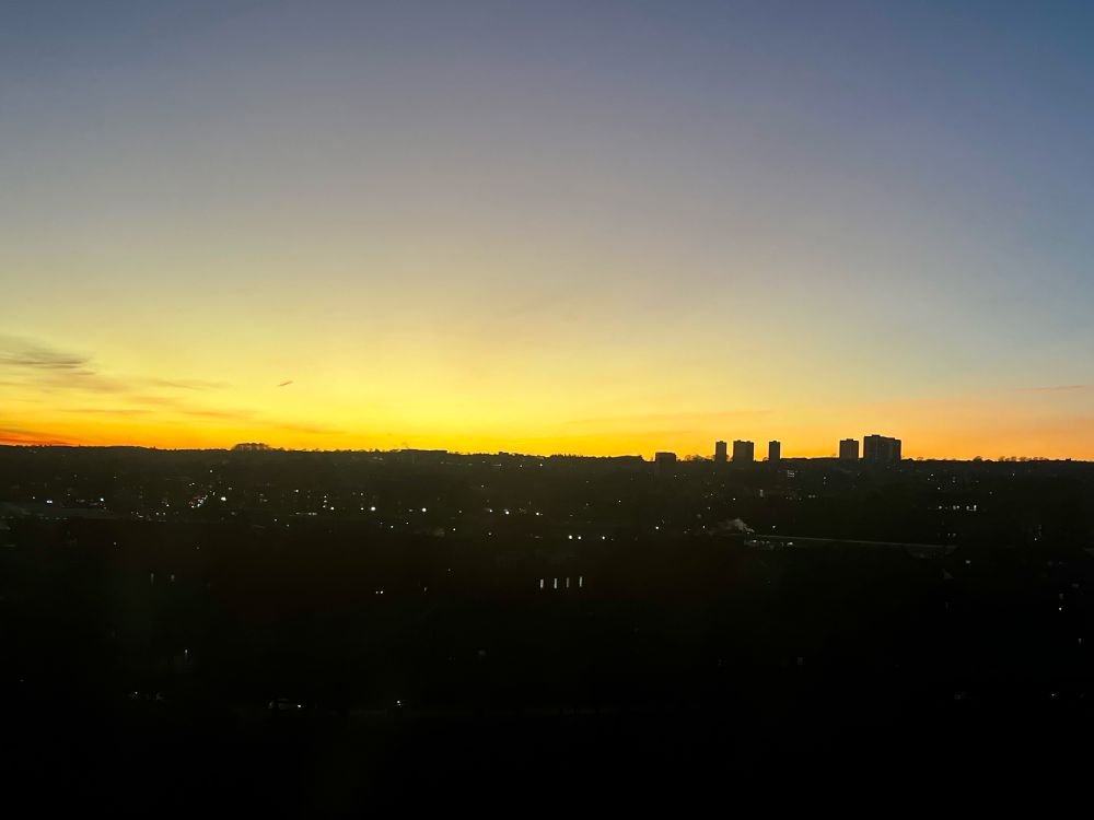 View from the top floor of The Sir Duncan Rice Library at sunset, with an orange, yellow and purple sky over a silhouette of the city skyline.