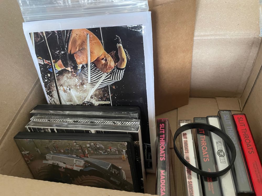 Shipping box containing various Slit Throats releases. Tapes ,CDs, lathe, stickers, wrist band & pins. Includes special packaged albums.