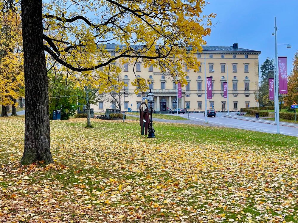 Yellow coloured Carolina Rediviva Uppsala University Library building with leaves on the ground in the foreground.