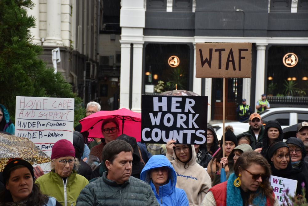 People holding signs that read 'Homecare and support are under-funded, undervalued, and under-paid', 'Her work counts' and 'WTAF'