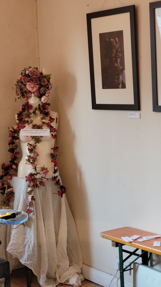A mannequin bedecked with flowers and wearing a mask covered with flowers, next to a photo of a similar subject.
