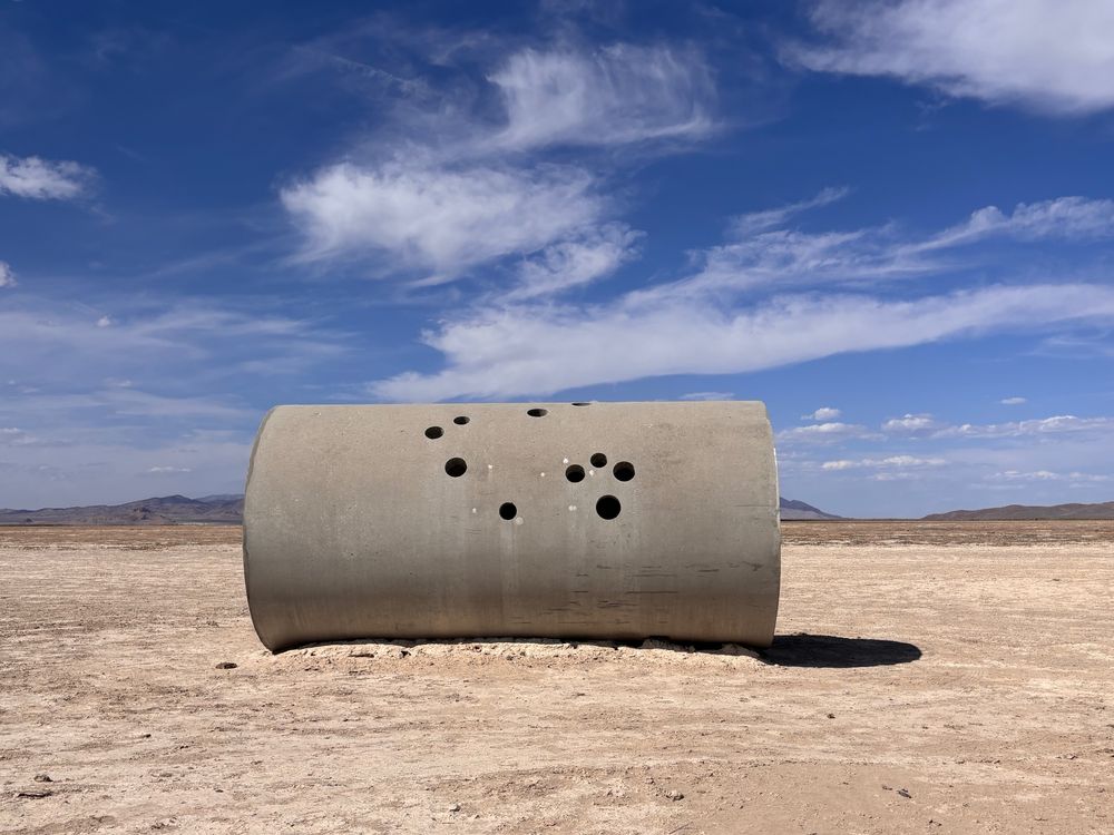 Sun Tunnel by Nancy Holt is a land art installation consisting of four large cement pipes. Each has holes corresponding to constellations. And they align with sunrise/set on the winter and summer solstices. This image shows the outside of a tunnel with its holes. In a wide open desert setting. 